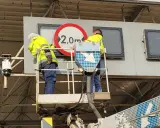 Pracownicy na podnośniku montują znak zakazu 2,0m, pokazując, jak działa e-toll.