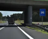 Droga jednojezdniowa pod wiaduktem, z ciężarówką i znakiem informującym o pasie ruchu dla samochodów.