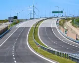Nowa droga S6 z wiatrakami w tle. Pusta autostrada z zielonym pasem zieleni i barierami.