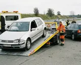 Pomoc drogowa w akcji: srebrny Volkswagen na lawecie, obok czarna Skoda i policja. Trwa holowanie auta po wypadku.