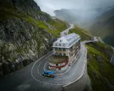 Malowniczy hotel na serpentynach w Alpach, idealny punkt na **grand tour szwajcaria**. Niebieski busik z panelami słonecznymi.