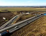 Rozbudowa autostrady A6 w otoczeniu pól i farm wiatrowych. Ruch samochodowy na ukończonych odcinkach, trwają prace budowlane.