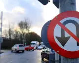 Znak zakazu zawracania informuje o nowych przepisach. Na mokrej drodze ruch samochodowy.