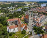 Zamek Piastów Śląskich w otoczeniu miasta i rzeki. Zabytkowa budowla z czerwonymi dachami, obok katedra z zielonymi wieżami.