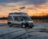 Srebrny kamper Globe-Traveller na tle zachodzącego słońca nad rzeką. Idealny wybór, jeśli zastanawiasz się, jaki kamper dla 2 osób sprawdzi się najlepiej na zimowe wyprawy.