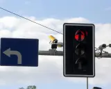 Rejestrator przejazdu na czerwonym świetle, widoczny na tle nieba, wraz z sygnalizacją świetlną i znakiem nakazu skrętu w lewo.