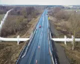 Droga krajowa 91 z wielkim białym rurociągiem biegnącym wzdłuż niej, otoczona drzewami i polami.