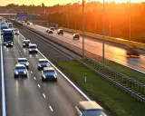 Zachód słońca nad Via Baltica. Samochody i ciężarówki pędzą autostradą w złotym blasku.
