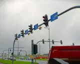 Na skrzyżowaniu wiszą sygnalizatory świetlne i znaki kierunkowe. Widać żółty tramwaj i czerwony wywrotkę. Gdzie są kamery rejestrujące przejazd na czerwonym świetle?
