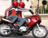 Dwie osoby w kaskach i kurtkach jadą na czerwonym motocyklu. Idealny na pierwsze prawo jazdy na 125.