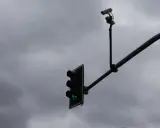Dwie białe kamery nad światłami sygnalizacji świetlnej, z zielonym światłem.