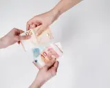 Dwie ręce przekazują sobie banknoty euro. W Austrii obowiązuje euro, co widać na przykładzie tych banknotów.