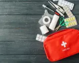 Czerwona apteczka z wyposażeniem: plastry, bandaże, nożyczki, termometr, strzykawki i tabletki. Czy trzeba mieć apteczkę w aucie? Tak, dla bezpieczeństwa!