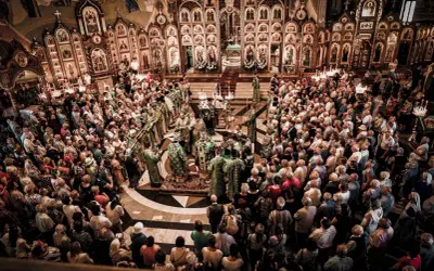 Uroczysta liturgia w największej cerkwi w Polsce. Wierni zgromadzeni wokół ikonostasu, duchowieństwo w bogatych szatach.