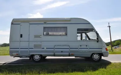 Biały ford galaxy camper z niebieskimi pasami stoi na poboczu drogi. W tle zielone pola i błękitne niebo.