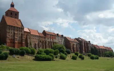 Zabytkowe miasto na trasie Ostróda-Grudziądz z ceglanymi budynkami i wieżą kościelną, otoczone zielenią i parkiem.