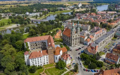 Zamek Piastów Śląskich w otoczeniu miasta i rzeki. Zabytkowa budowla z czerwonymi dachami, obok katedra z zielonymi wieżami.