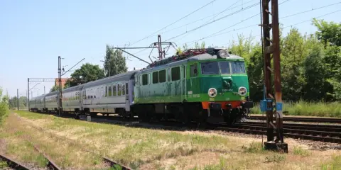 Zielony pociąg EU07-052 z wagonami mija tory w słoneczny dzień. To widok z wieluń trasa.