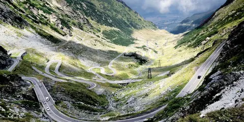 Kręta trasa Transfogarska w Rumunii, wijąca się przez górzysty krajobraz. Samochody pokonują liczne zakręty, podziwiając malownicze widoki.