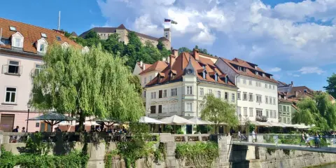 Urokliwy widok na rzekę i zabytkowe kamienice w Słowenii, Lublana. W tle widać zamek na wzgórzu.