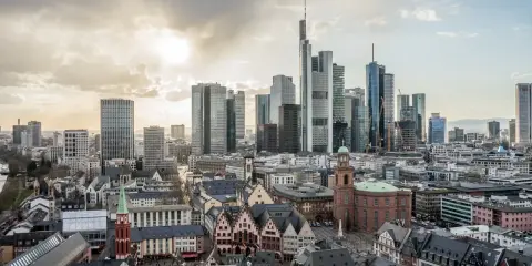 Widok na nowoczesne i zabytkowe frankfurt nad menem dzielnice, z drapaczami chmur i kościołami pod zachodzącym słońcem.