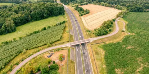 Nowa sól trasa przecina zielone pola i lasy, łącząc odległe zakątki. Widok z lotu ptaka ukazuje drogę, most i samochody w ruchu.