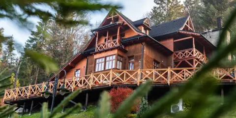 Drewniane schronisko turystyczne z tarasem i balustradą, otoczone drzewami.