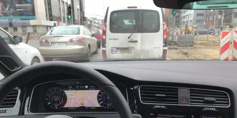 Utrudnienia na drodze, korek przed budową. Samochody stoją w deszczu, nawigacja pokazuje objazd.