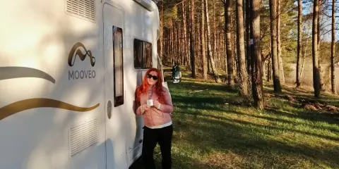 Kobieta z kubkiem kawy przy kamperze w lesie. Wspaniała przygoda z kamperem w Finlandii.