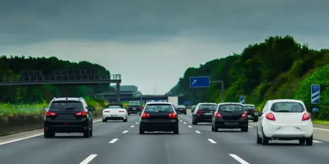 Ruch samochodów na niemieckiej autostradzie A8 pod pochmurnym niebem. Widać kilka czarnych i jeden biały samochód jadący pasem.