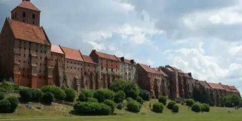 Zabytkowe miasto na trasie Ostróda-Grudziądz z ceglanymi budynkami i wieżą kościelną, otoczone zielenią i parkiem.