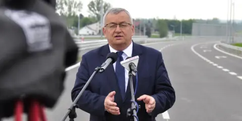 Mężczyzna w garniturze przemawia do mikrofonów na tle nowej drogi, która połączy Lublin i Rzeszów.