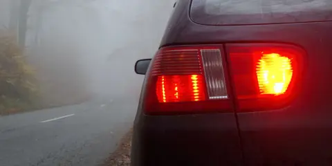 Czerwone światła stopu i włączone przeciwmgielne przednie samochodu na mglistej drodze w lesie.