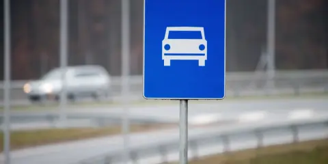 Znak drogowy szybkiego ruchu z symbolem samochodu. W tle widać rozmazany pojazd na drodze.