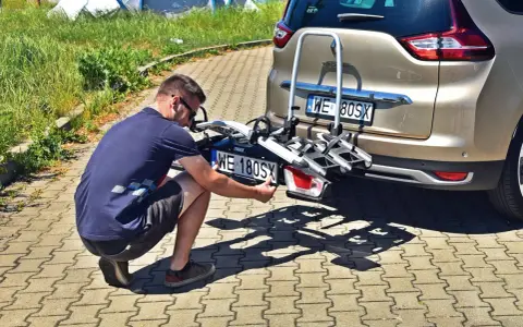 Mężczyzna montuje trzecią tablicę rejestracyjną WE 180SX na bagażniku rowerowym przy samochodzie.