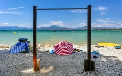 Słoneczne plaże nad jeziorem Garda, z parasolami, leżakami i wodnymi atrakcjami w tle.