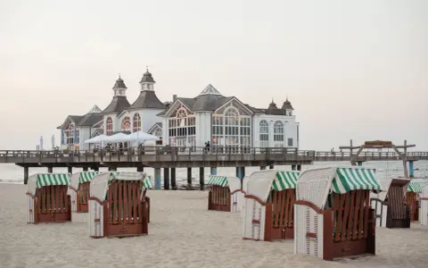 Plaża na wyspie Rugia z charakterystycznymi koszami plażowymi i molo prowadzącym do białego pawilonu.