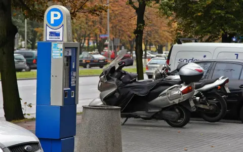 Parkomat z symbolem "P" i skuterem obok. Upewnij się, że masz ważny bilet, by uniknąć mandatu za parkowanie.