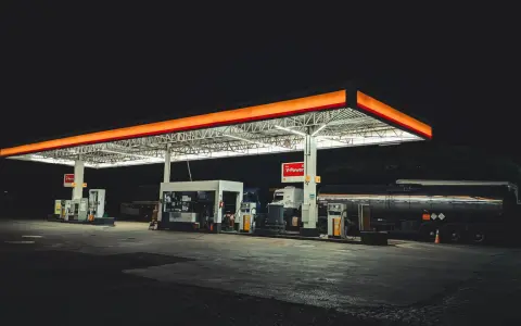 Nocna stacja paliw w Polsce, oświetlona neonami, z dystrybutorami i cysterną.