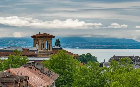 Widok na szwajcarskie miasto nad jeziorem Genewskim, z charakterystyczną wieżą i dachami budynków.