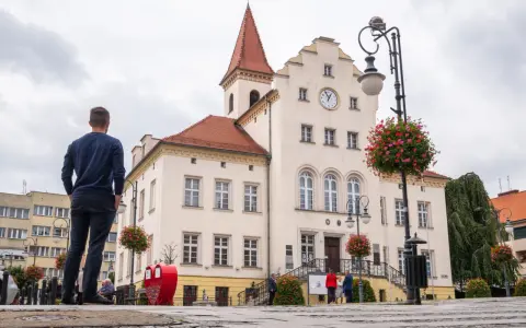 Mężczyzna stoi na rynku w Trzebnicy, podziwiając zabytkowy ratusz. Trasa spacerowa przez miasto prowadzi obok pięknych budynków.