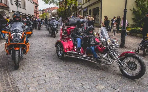 Parada motocykli i trójkołowców na brukowanej ulicy. W tle widzimy ludzi i budynki. To może być początek podróży szwecja motocyklem.