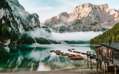 Spokojne jezioro w Dolomitach, Tyrol Włochy, z łodziami przy drewnianym molo i mgłą otulającą góry.