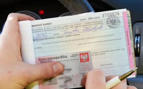 Ręka trzyma mandat karny na kwotę 300 zł. Obok dowód osobisty. Jak uniknąć mandatu? Uważaj na drodze!