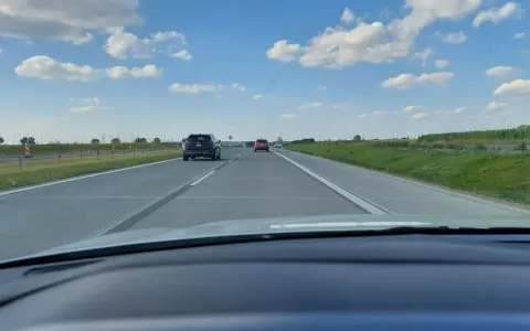 Jadąc na S7, widzimy pola i chmury. Samochody poruszają się po pustej drodze.