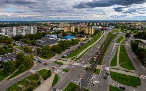 Widok z lotu ptaka na ruchliwe skrzyżowanie w Gdańsku Chełmie, z tramwajem, samochodami i budynkami mieszkalnymi w tle.