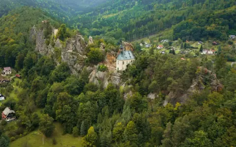 Malowniczy kościółek na skale, otoczony lasami, to jedno z **ciekawych miejsc w Czechach**. W oddali widać domki w dolinie.