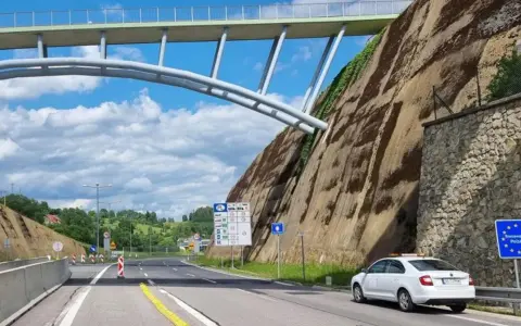 Biały samochód na granicy Polski, przygotowuje się do podróży do Danii samochodem. Nad drogą wznosi się imponujący most.