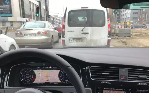 Utrudnienia na drodze, korek przed budową. Samochody stoją w deszczu, nawigacja pokazuje objazd.