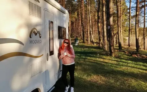 Kobieta z kubkiem kawy przy kamperze w lesie. Wspaniała przygoda z kamperem w Finlandii.